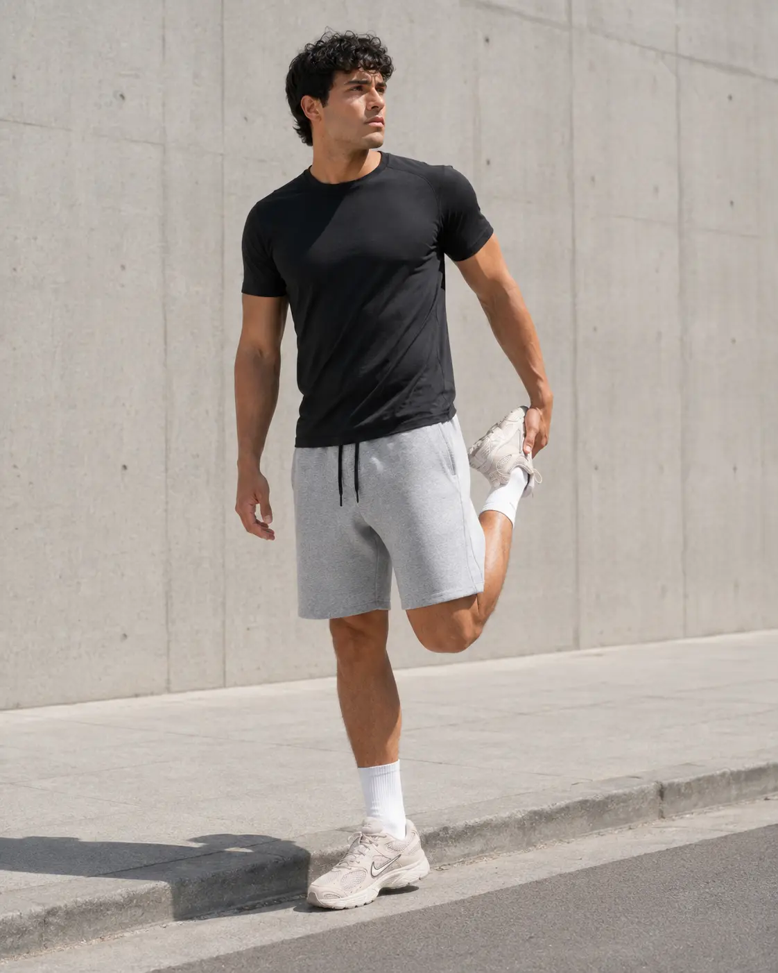 Model stretching a quad at the curb in grey training shorts and Nike V5 RNR trainers