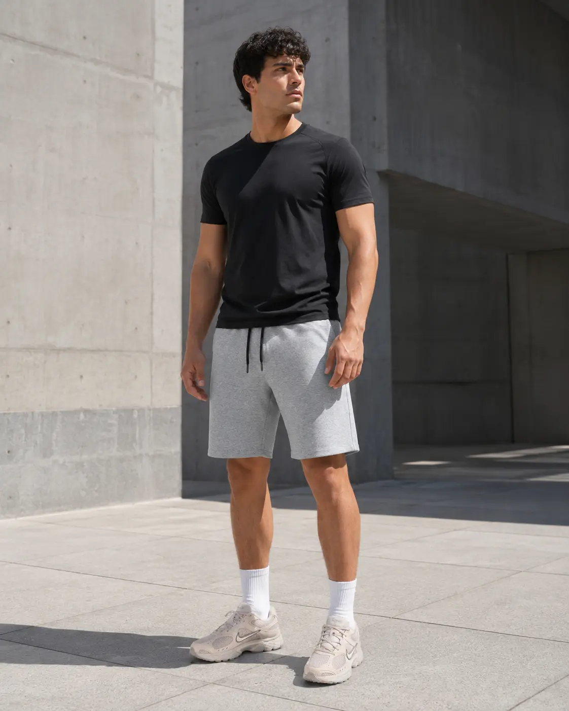Model in black tee, grey training shorts and Nike V5 RNR trainers on a concrete plaza