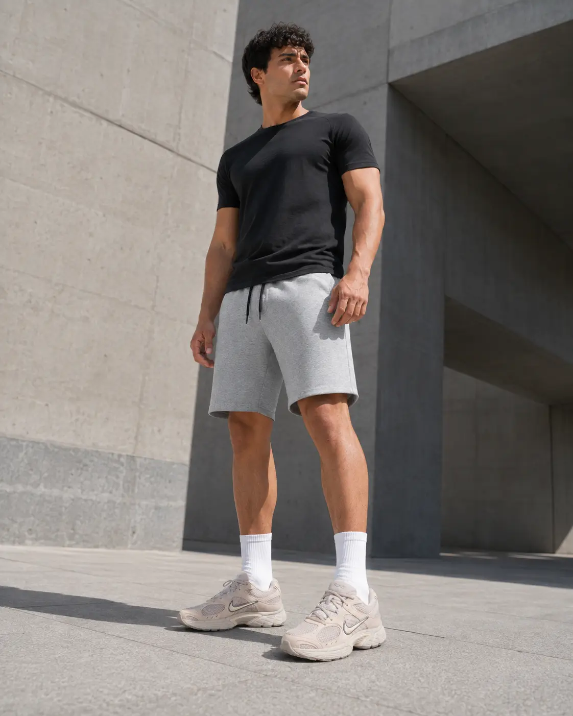 Low-angle shot of grey training shorts and Nike V5 RNR trainers against concrete architecture