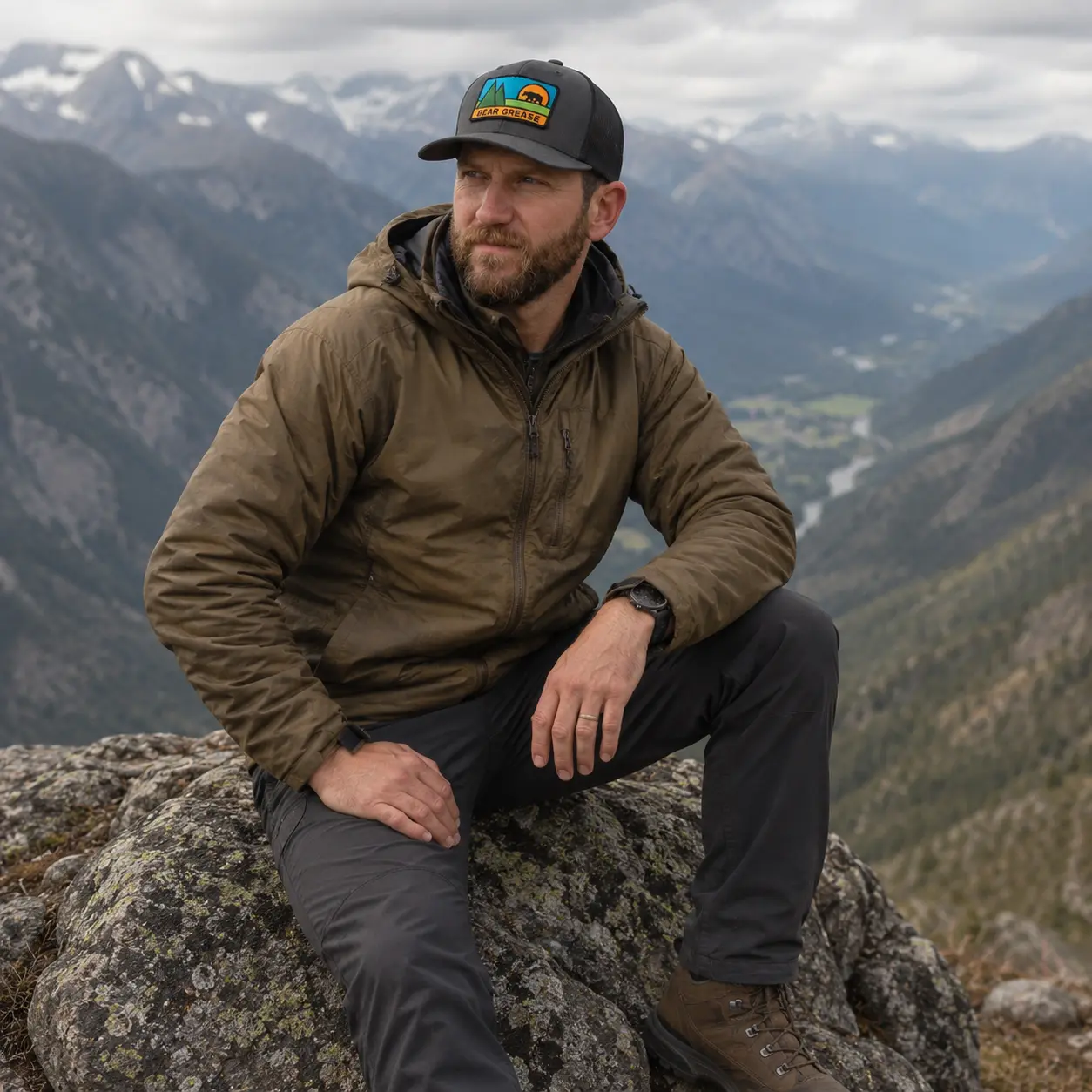 Model seated on a granite boulder above a valley wearing the Bear Grease trucker hat
