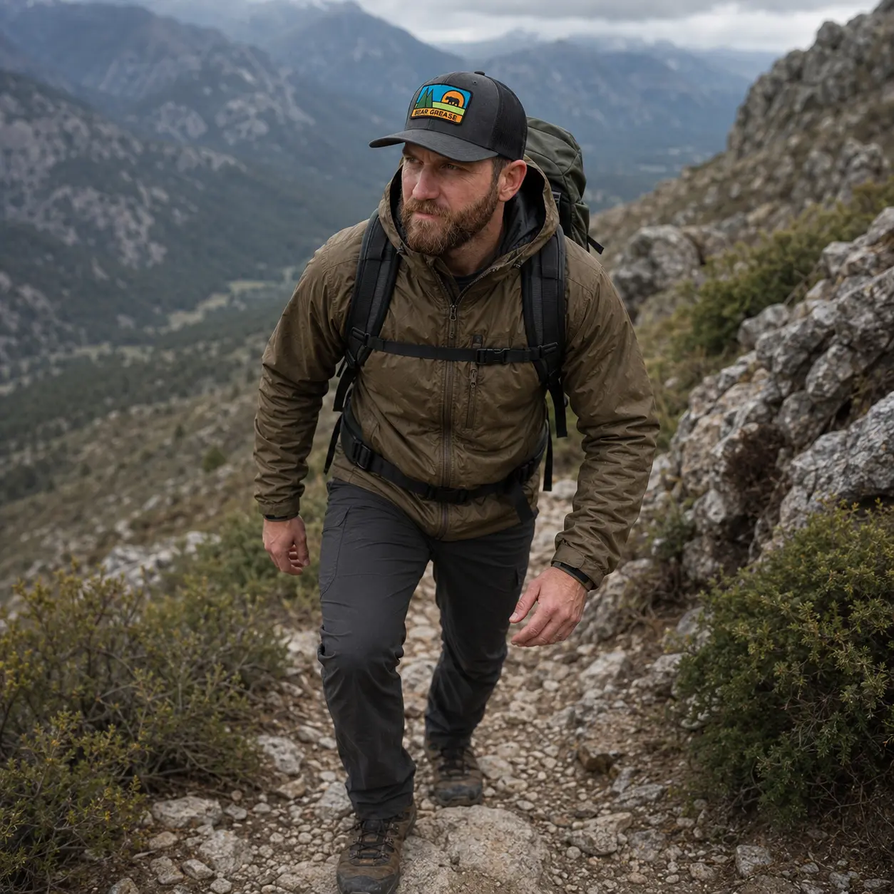Model hiking a rocky mountain trail wearing the Bear Grease trucker hat and a pack