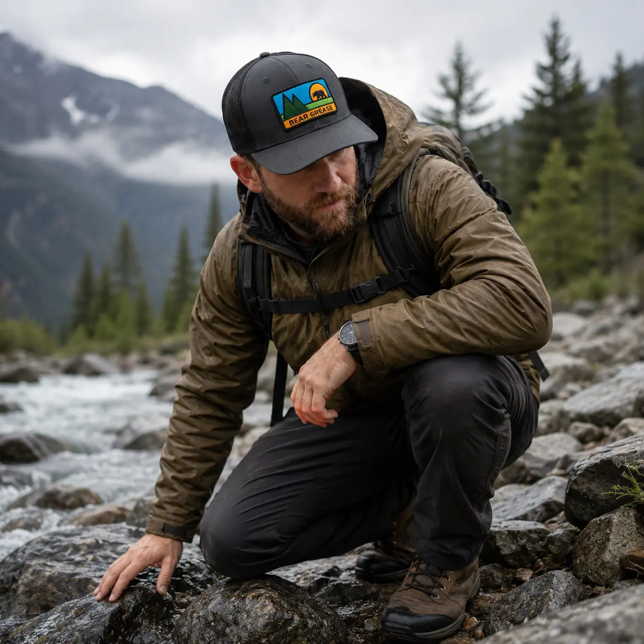 Model kneeling beside a rushing mountain creek wearing the Bear Grease trucker hat