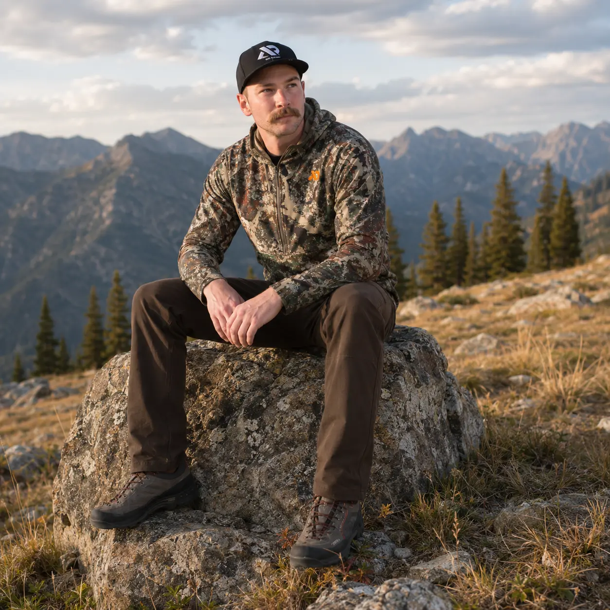 Model resting on a boulder above treeline wearing the Navigator Hoody