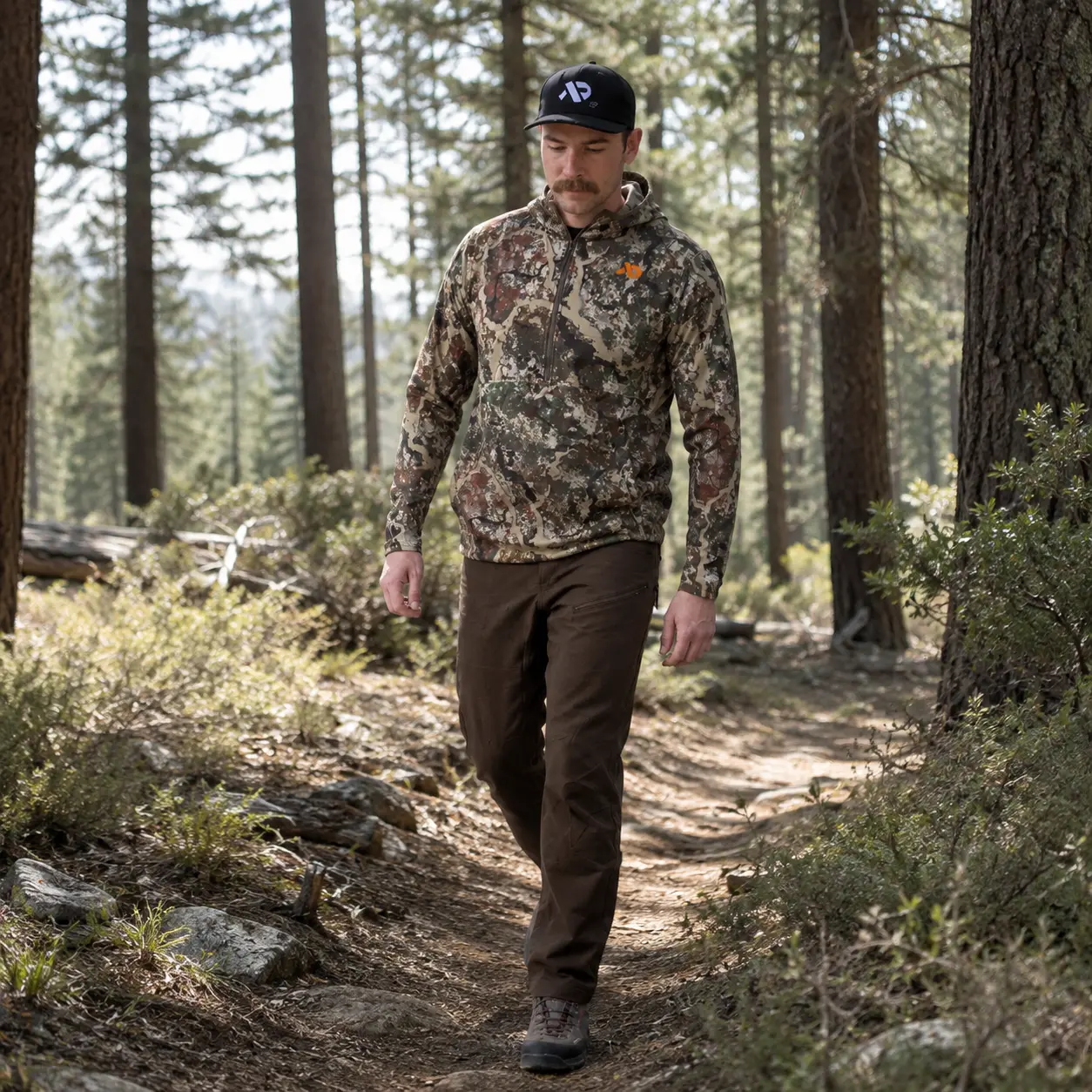 Model walking a pine forest trail in the Navigator Hoody in dappled light