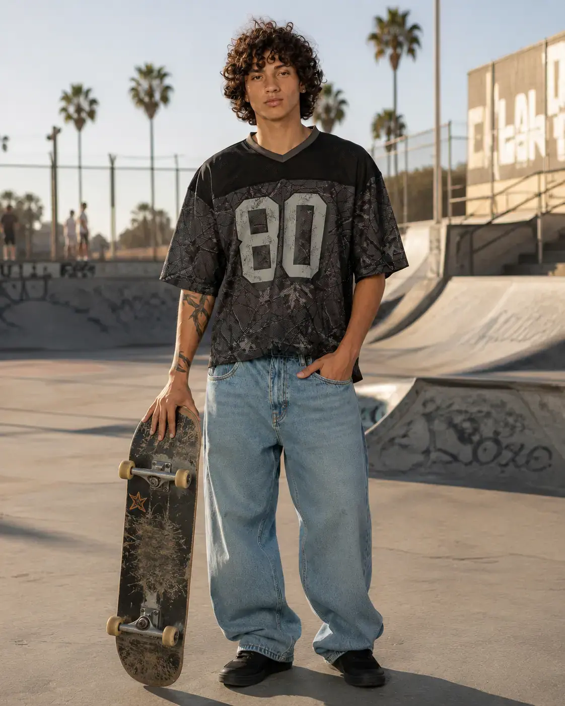 Man in a black number 80 mesh jersey holding a skateboard at a palm-lined skatepark
