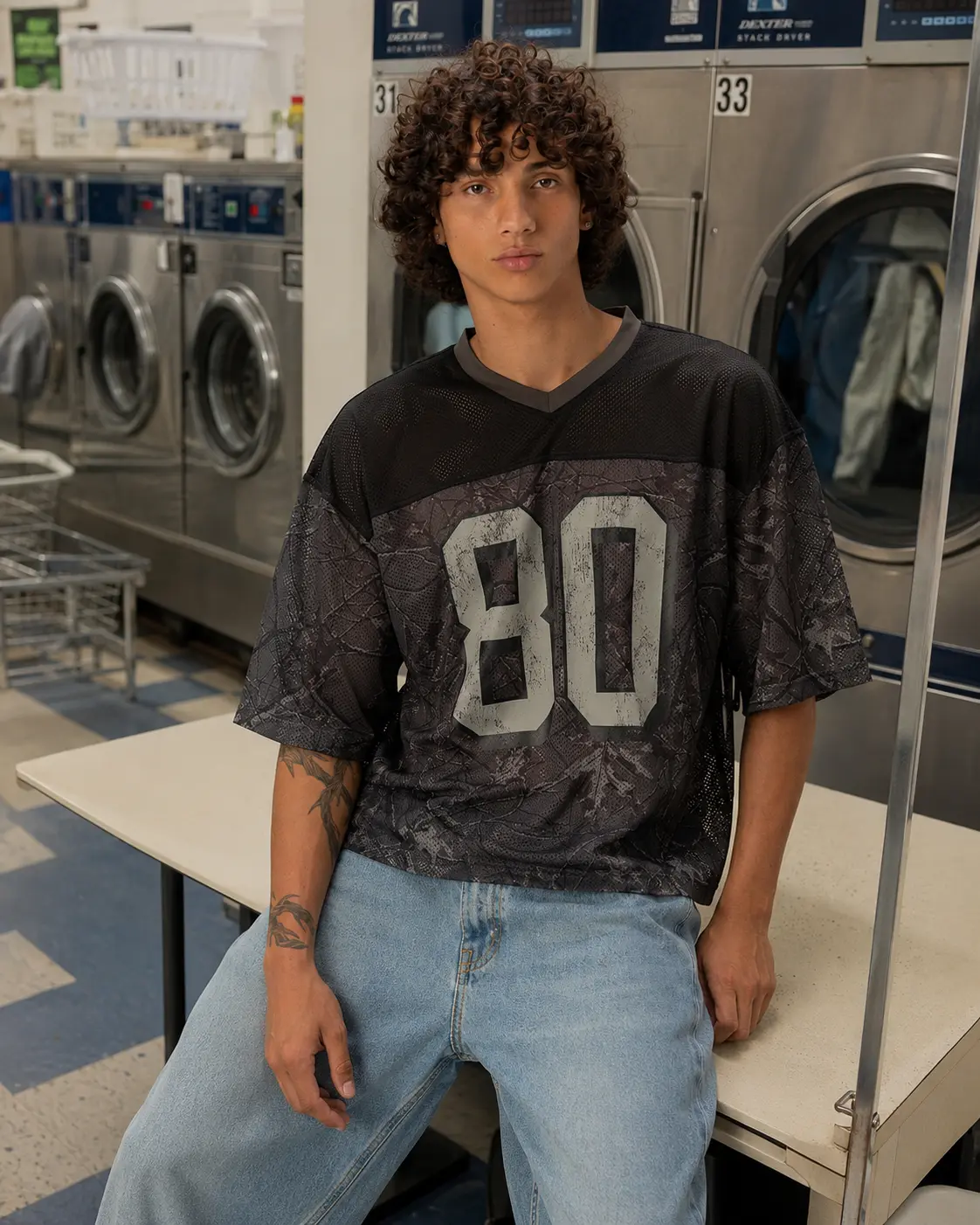 Man in a mesh jersey leaning on a table in a laundromat