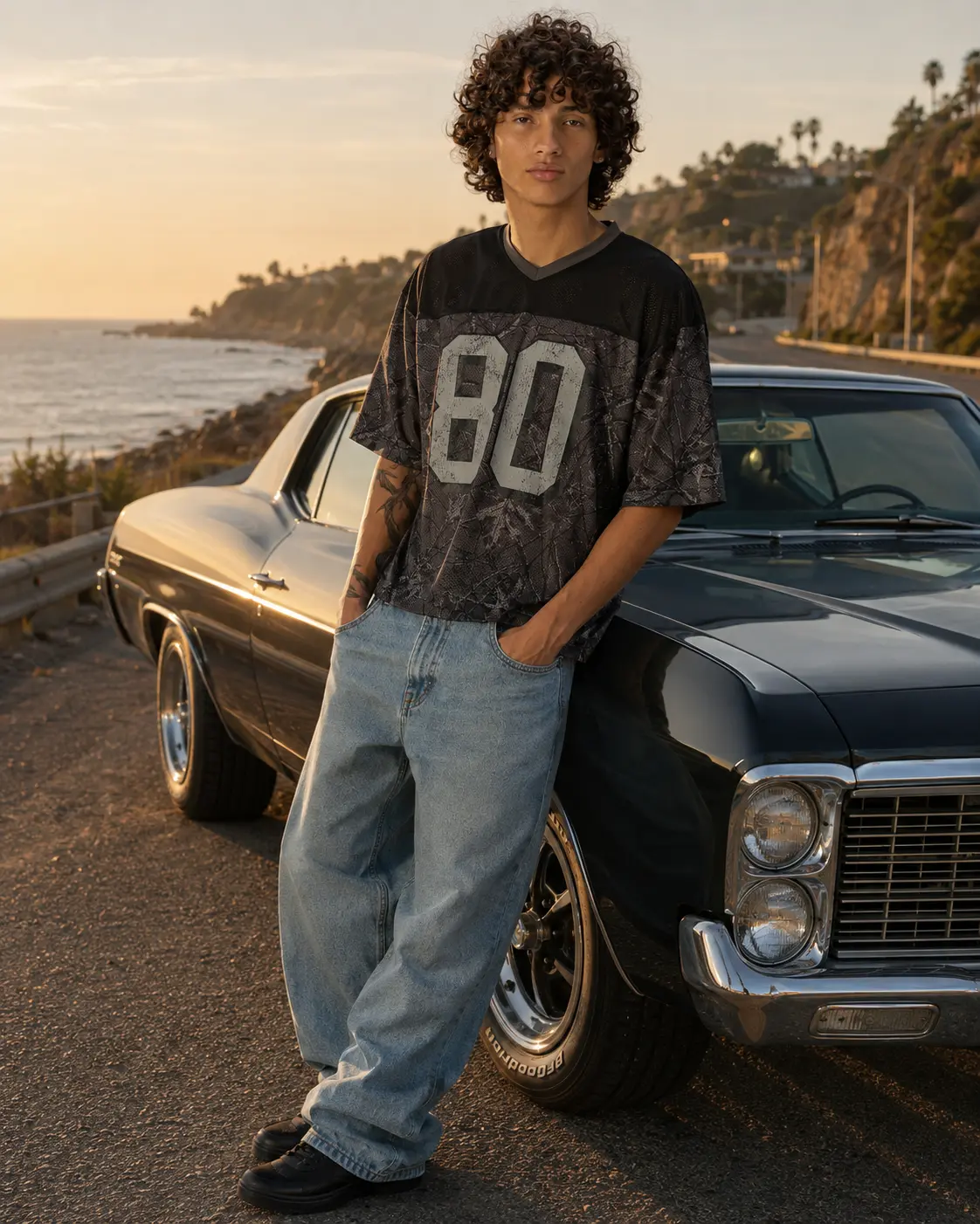 Man in a black number 80 mesh jersey leaning on a classic car on the coast at sunset