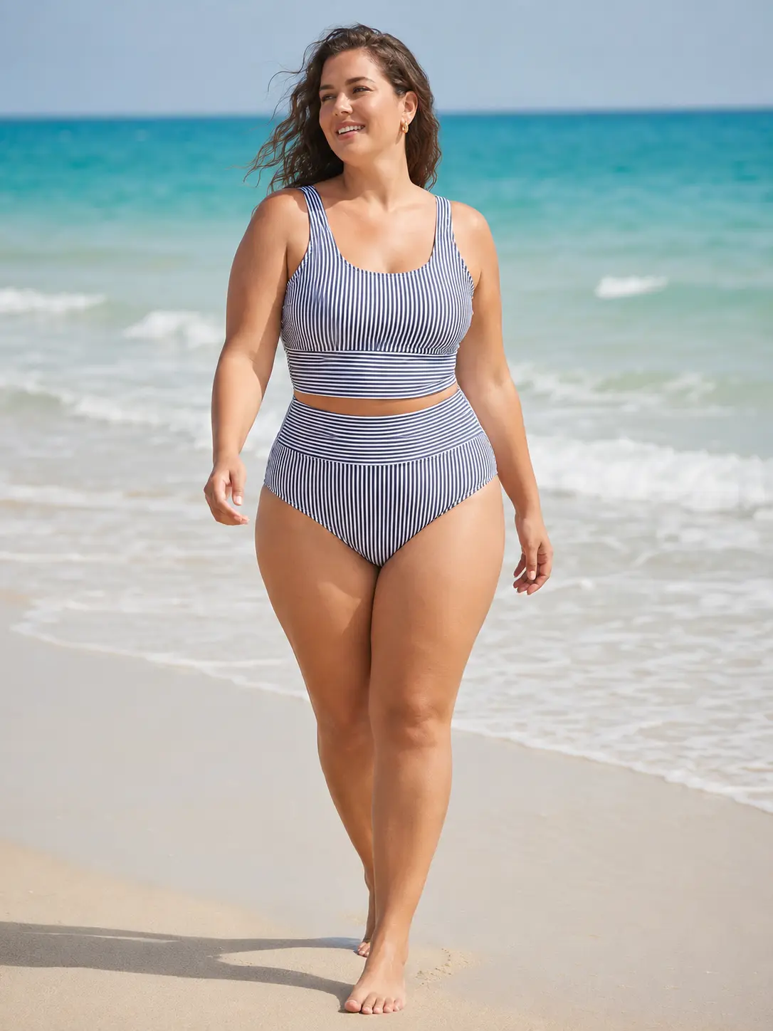 Model walking the shoreline in a navy striped swim set