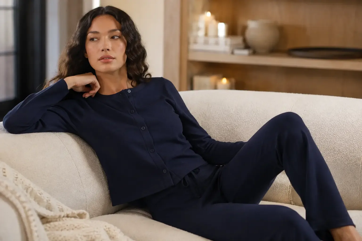 Model reclining on a cream bouclé sofa in a navy cardigan set